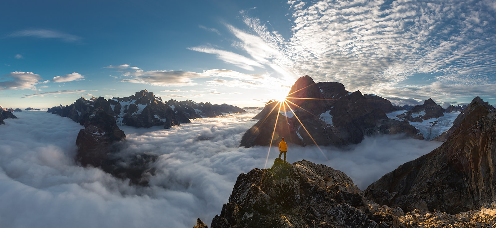 Chris Zielecki standing on a summit in Greenland watching sunset