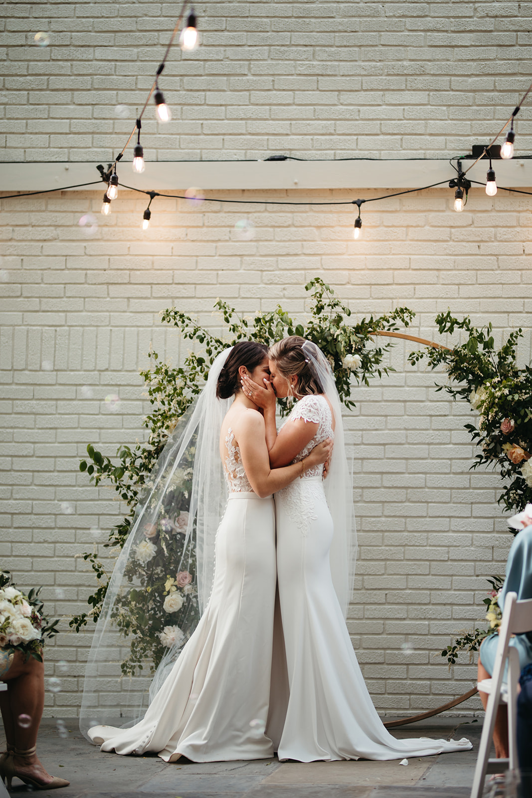 Two brides in dresses kissing at wedding ceremony
