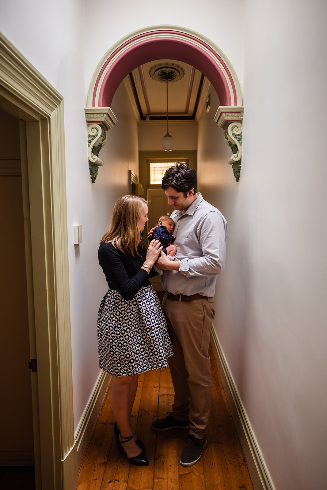 new parents standing in hall way at home holding their newborn daughter
