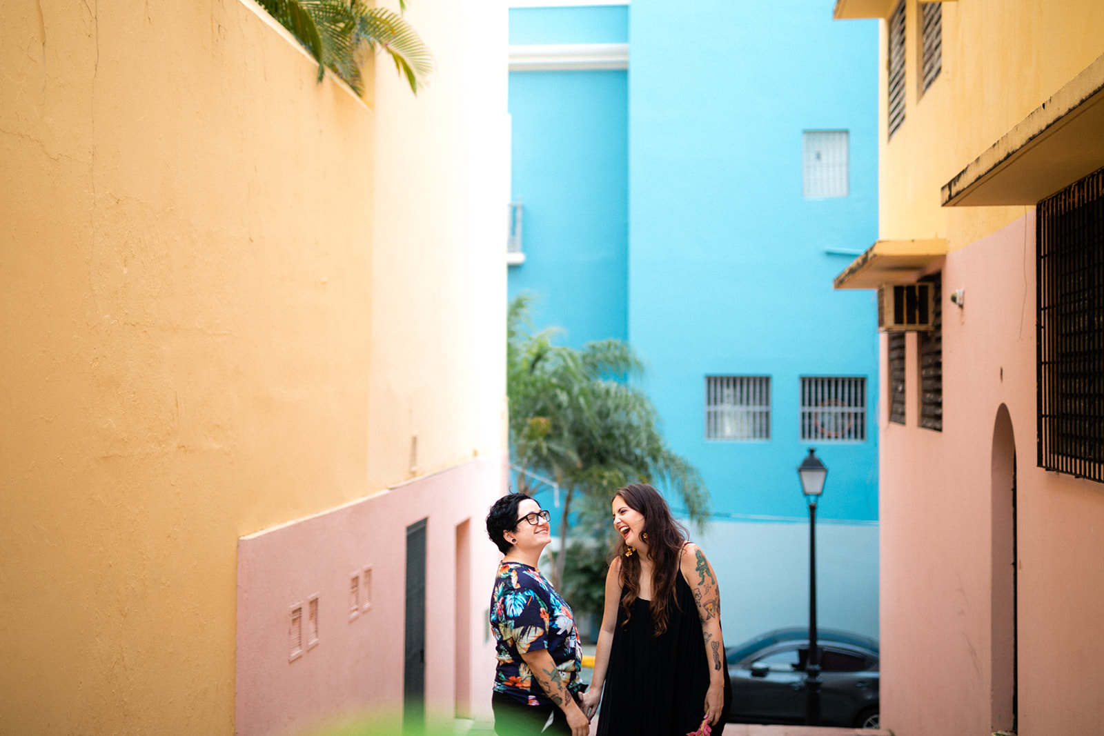 A cute queer couple laughs together surrounded by colorful buildings in Old San Juan.