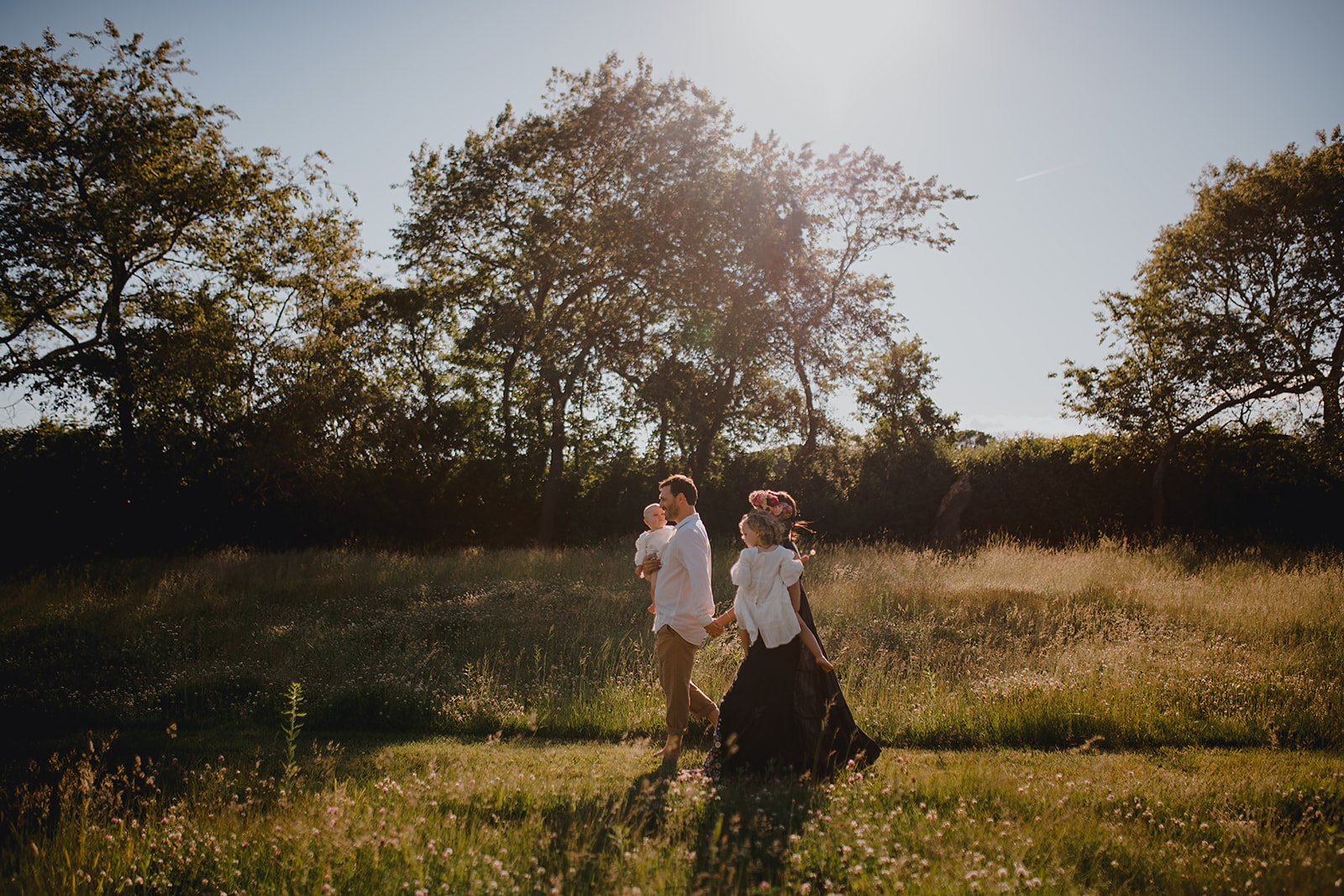 Bride and groom holding hands in a sun-kissed meadow with tall trees in the background