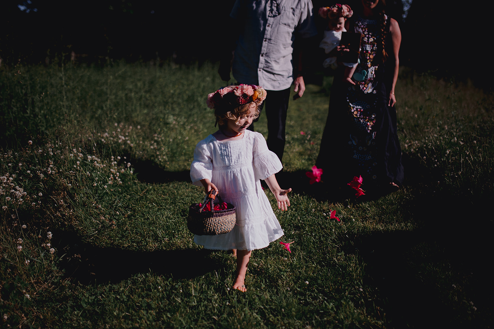 Red petals contrasted against green grass being thrown by five year old flower girl walking in field.
