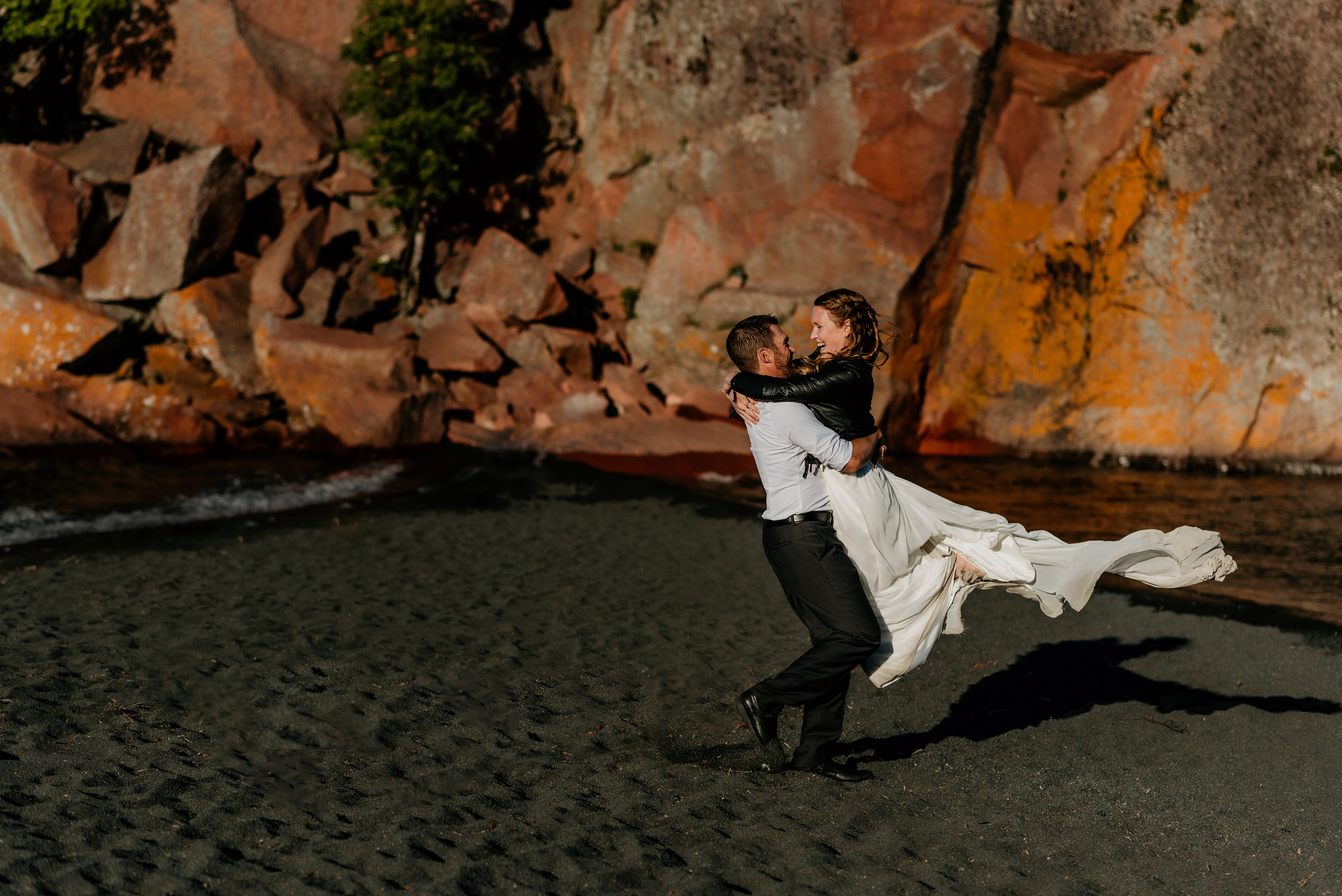 groom lifting bride and spinning her around on a black sand beach in minnesota