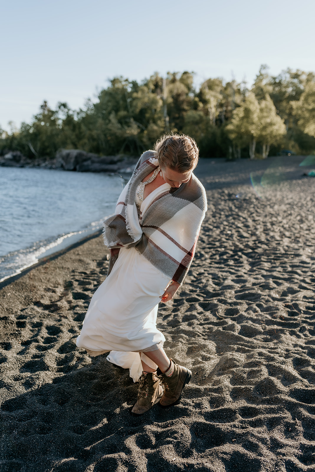 bride in white dress and wrapped in blanket on black sand beach in minnesota