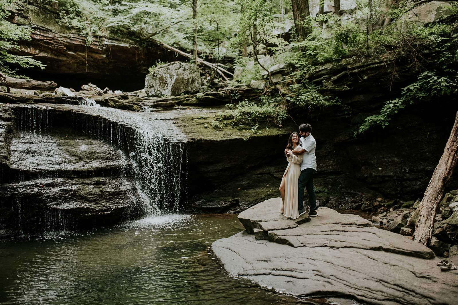 couple standing on rock kissing with waterfall behind