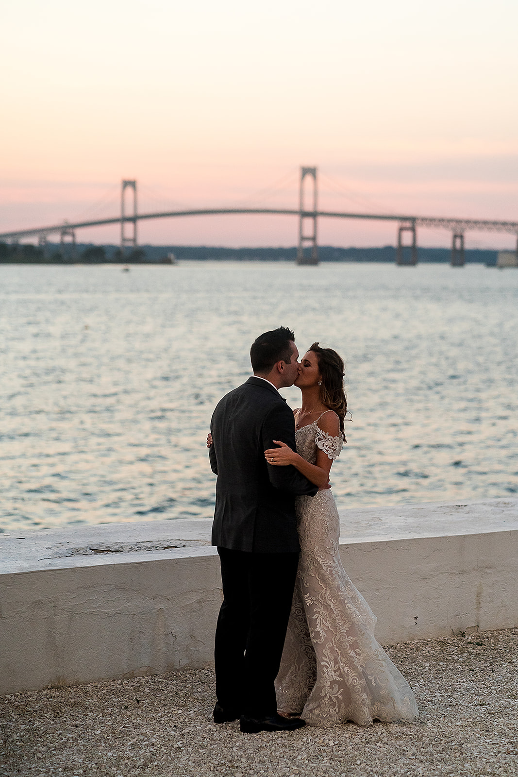 bride and groom kiss at sunset with Newport bridge in the background at belle mer