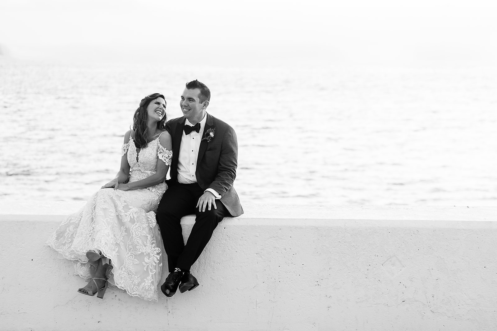 bride and groom laugh while sitting on waterfront at belle mer
