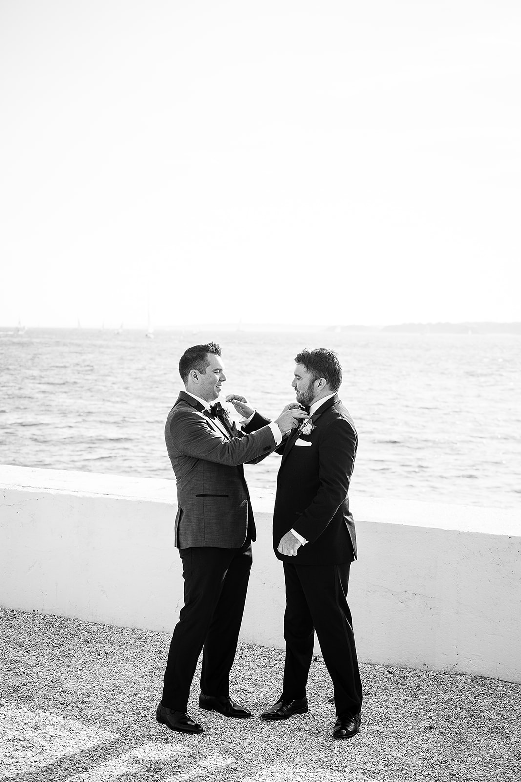 groom and brother help each other adjust their bow tie at the same time during family photos at belle mer