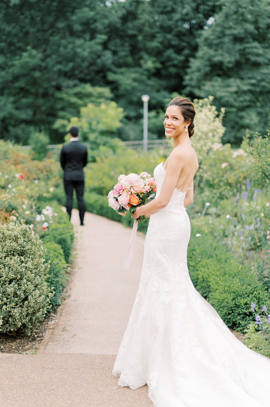 bride looks back before first look with groom in flowers at parisian inspired peachy Bartram's Garden wedding