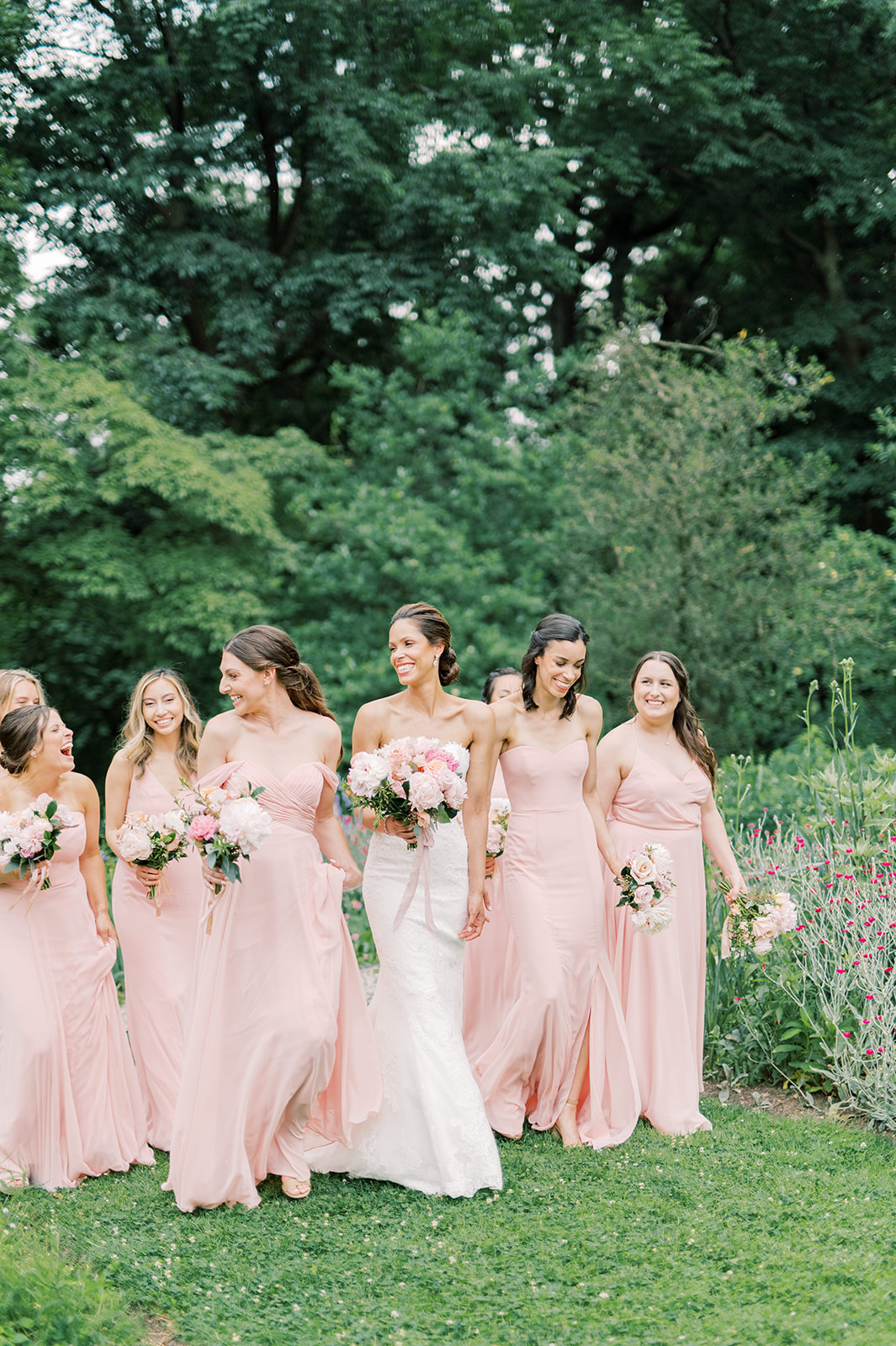 bridesmaids walk happily in pink dresses for this peachy parisian inspired spring Bartrams' Garden wedding in Philly, PA