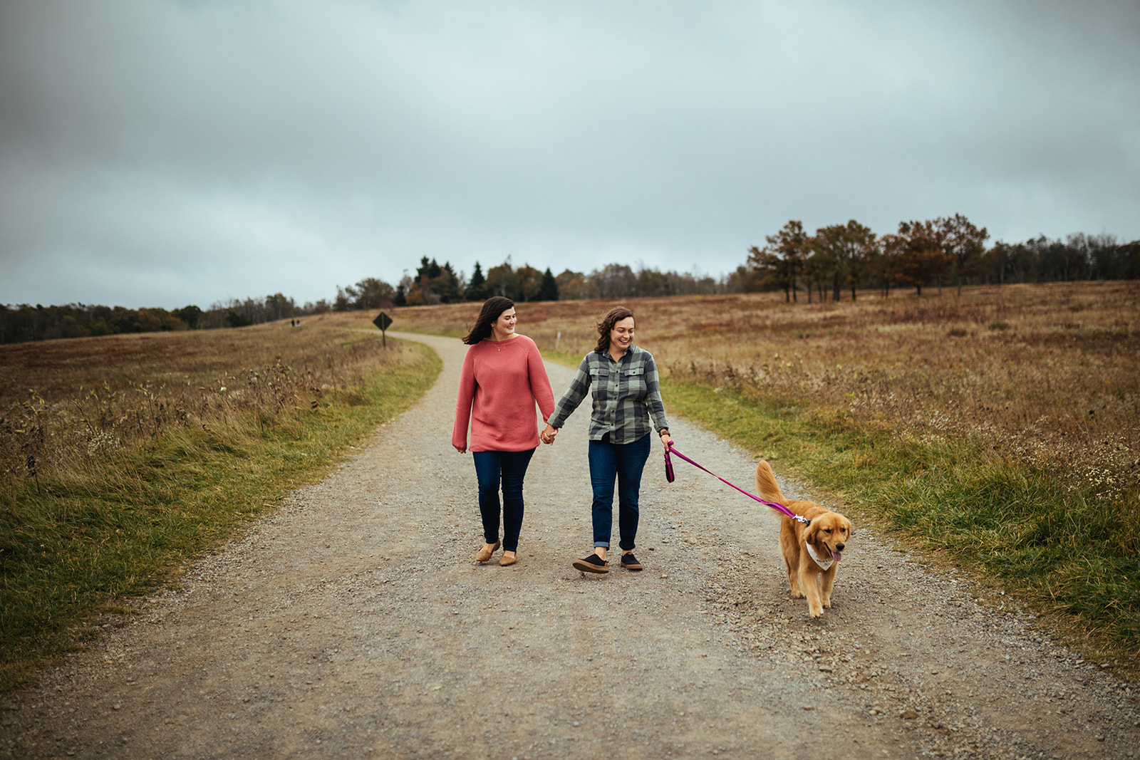 Two women walking holding hands with their golden retriever in Shenandoah National park