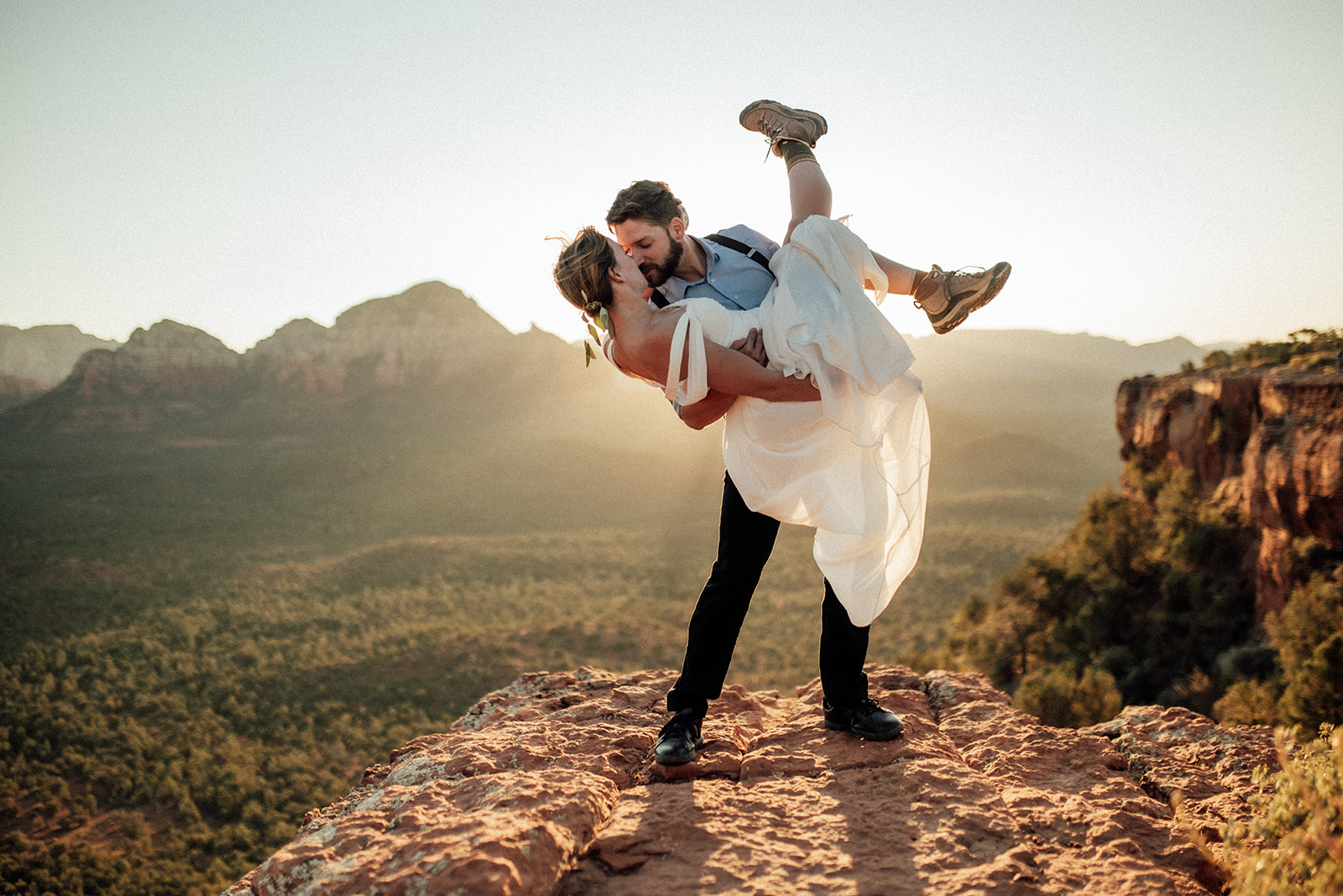 groom holding bride on cliff with sunrise behind