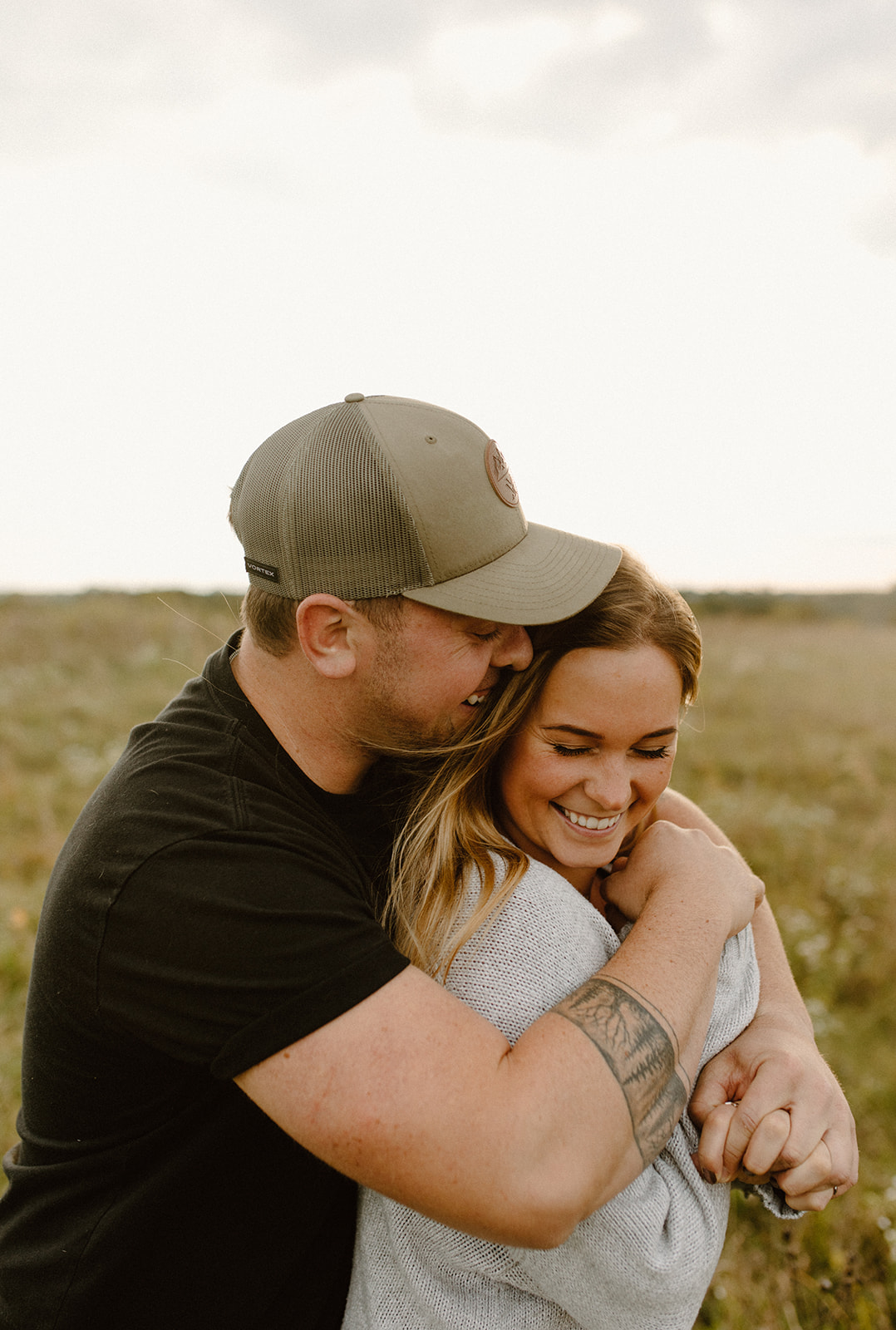 a couple in a grassy field at golden hour hugging during a photo session