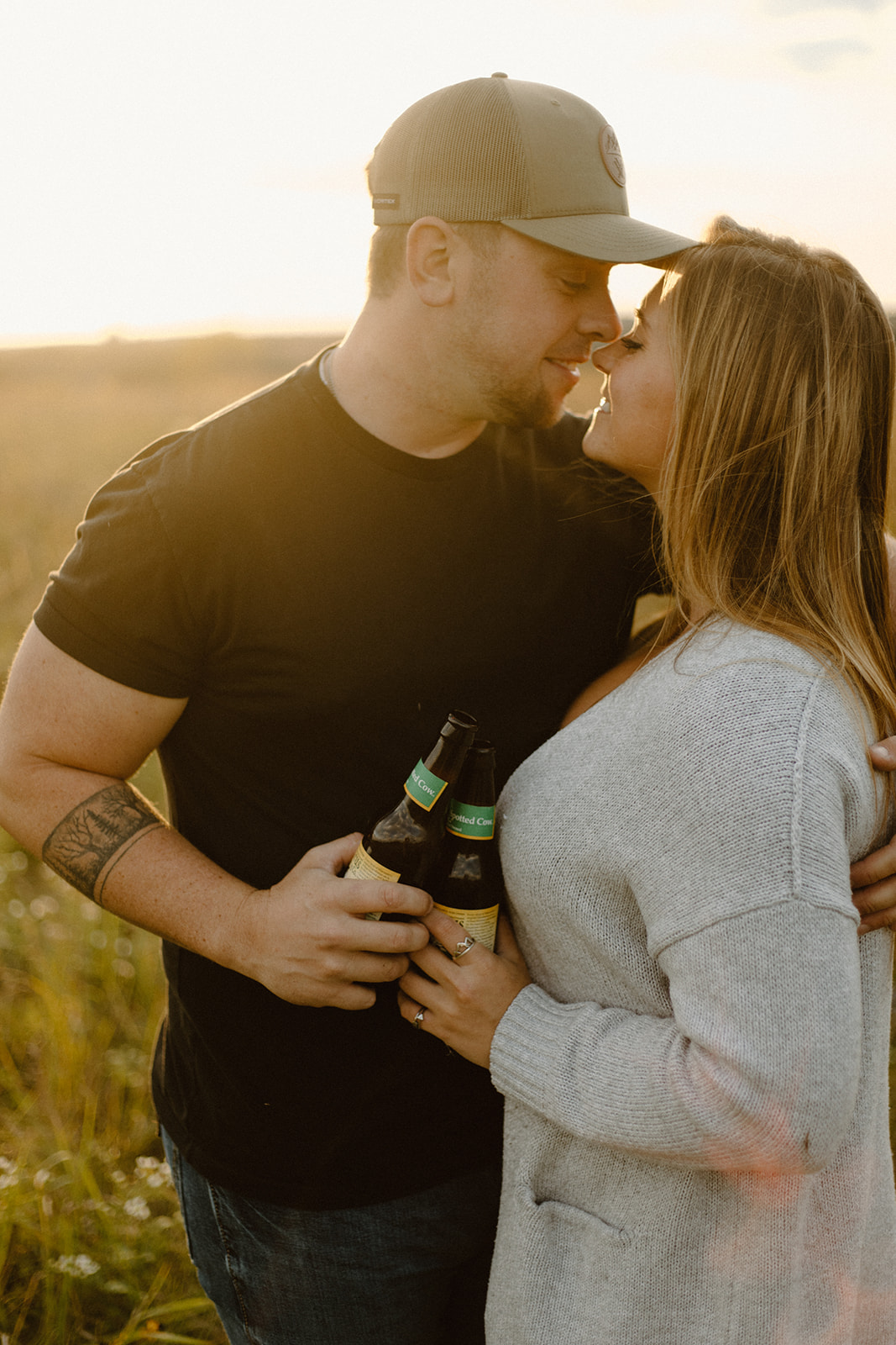 a couple in a grassy field with spotted cow beer bottles at golden hour during a photo session in barneveld, wisconsin 