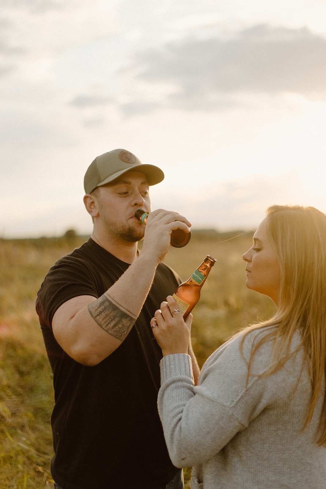 a couple in a grassy field with spotted cow beer bottles at sunset during a photo session in barneveld, wisconsin 