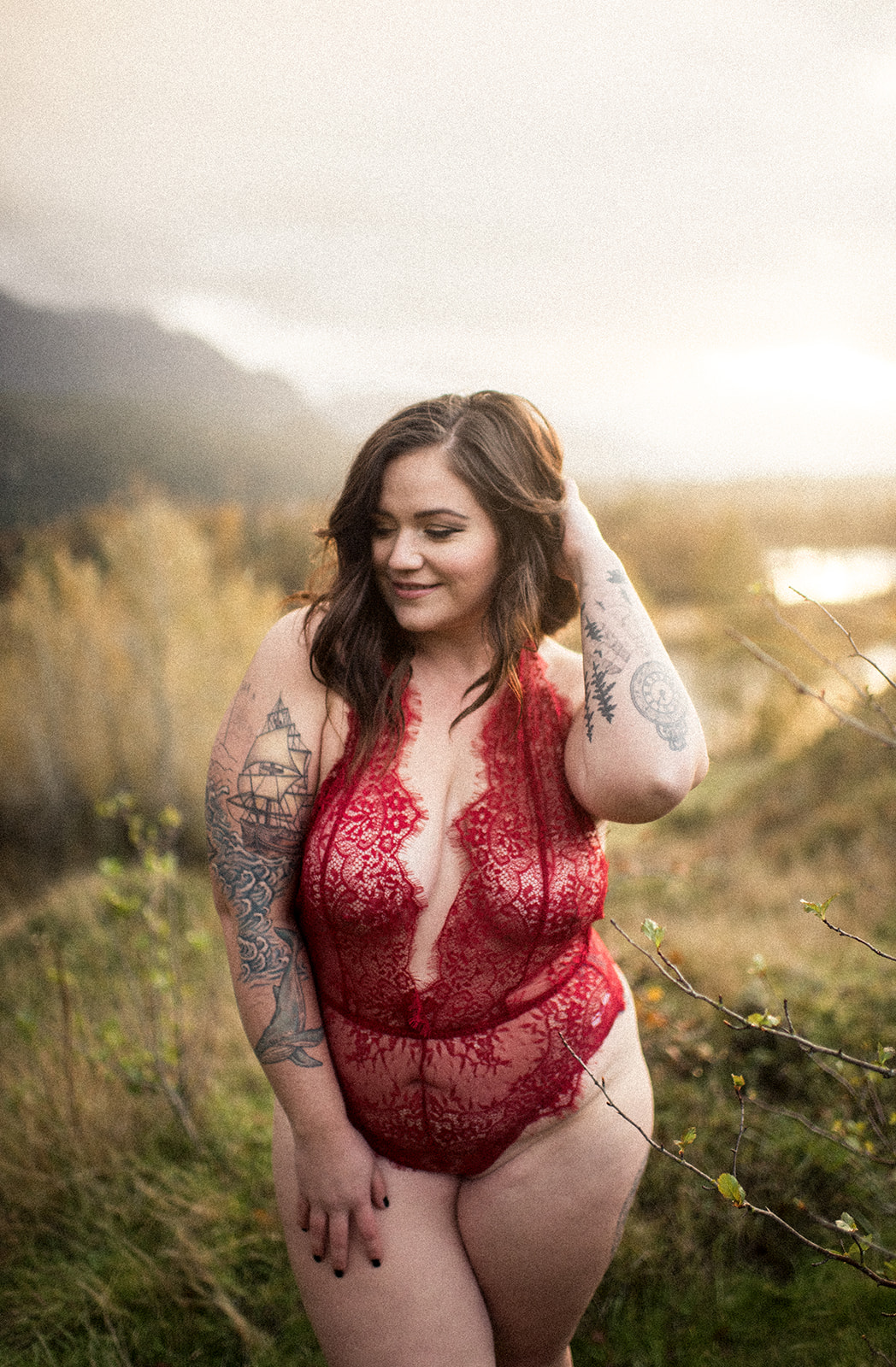 woman with brown hair wears red lingerie and smiles for her boudoir session on the columbia river gorge