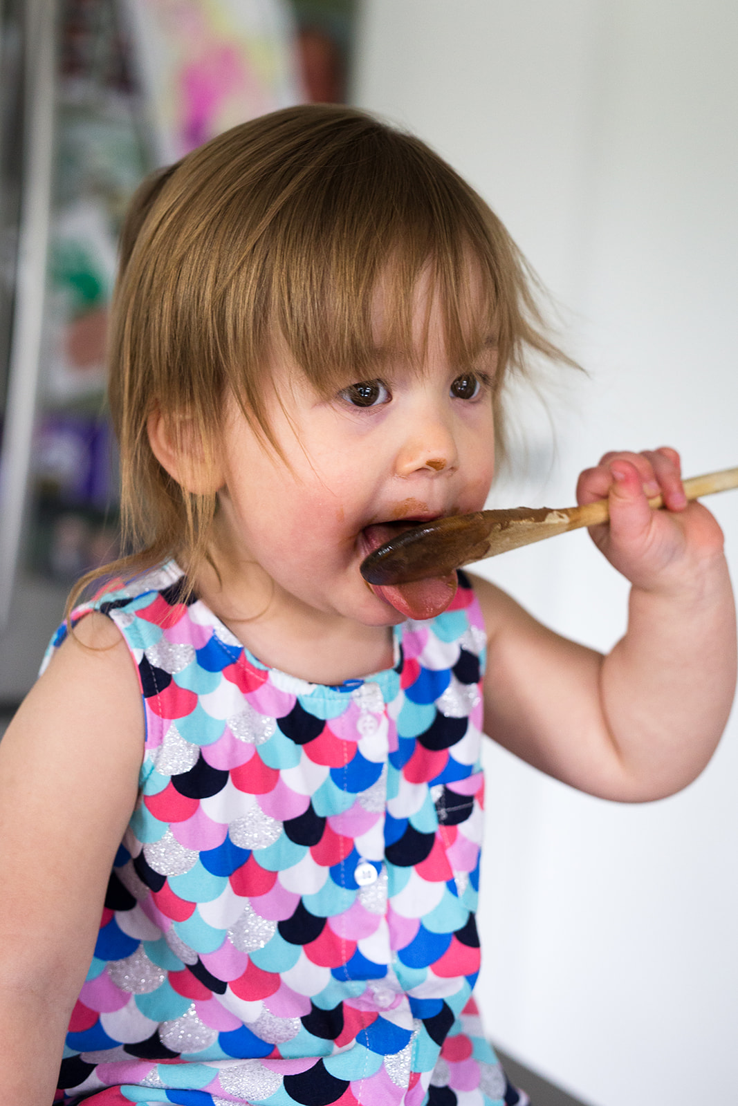 toddler eating cake batter off a wooden spoon