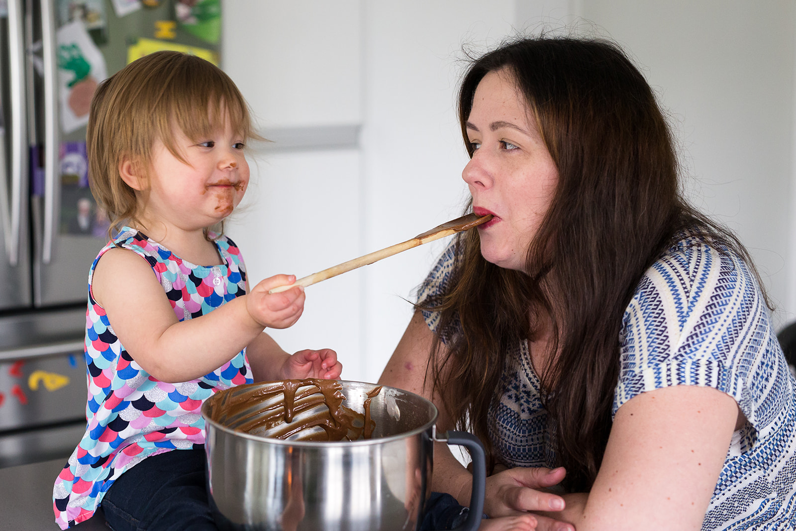 toddler feeding cake batter to her mother