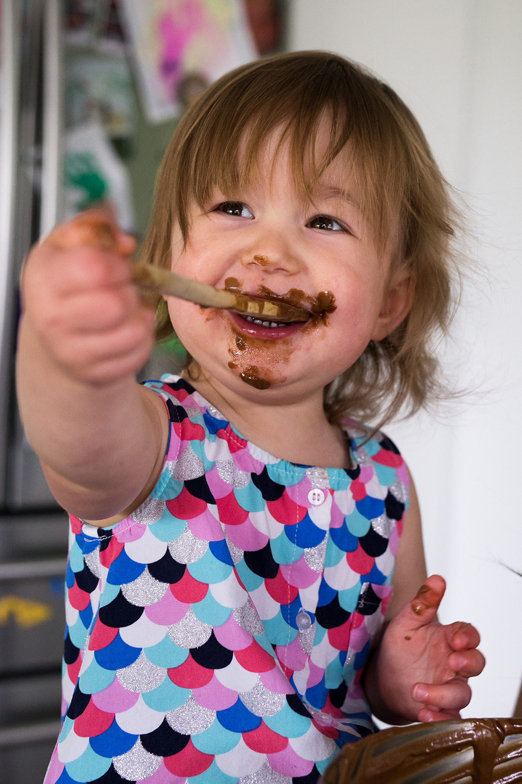 toddler smiling while licking a wooden spoon