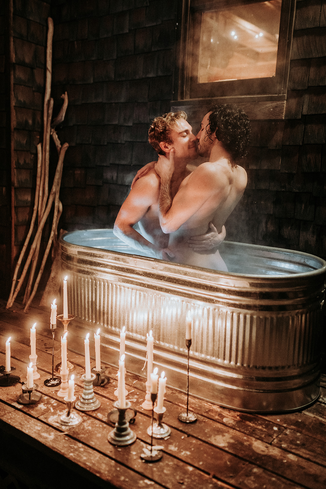 Two gay guys kissing in a hot tub surrounded by candlelight.