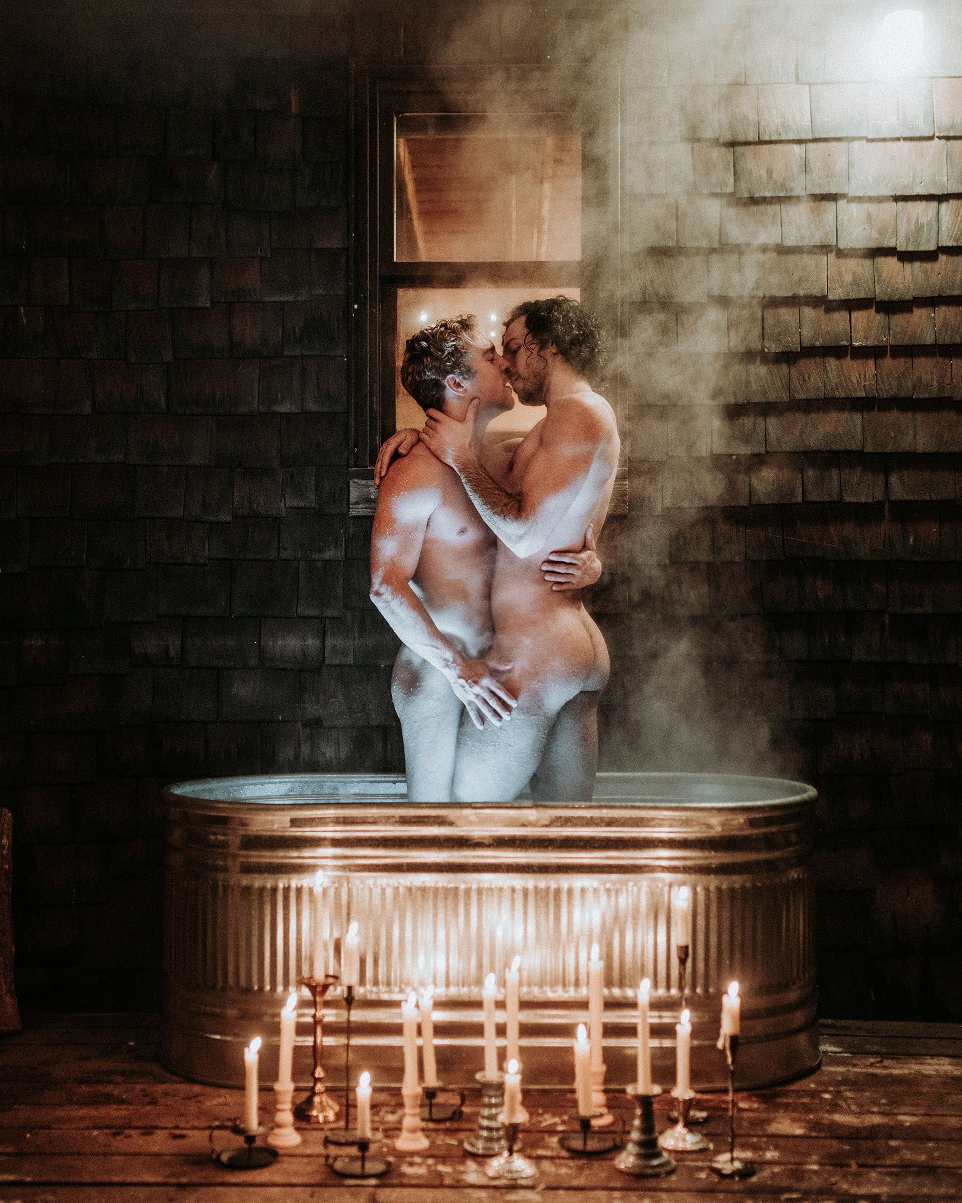 Two gay men kissing in a hot tub surrounded by candles.