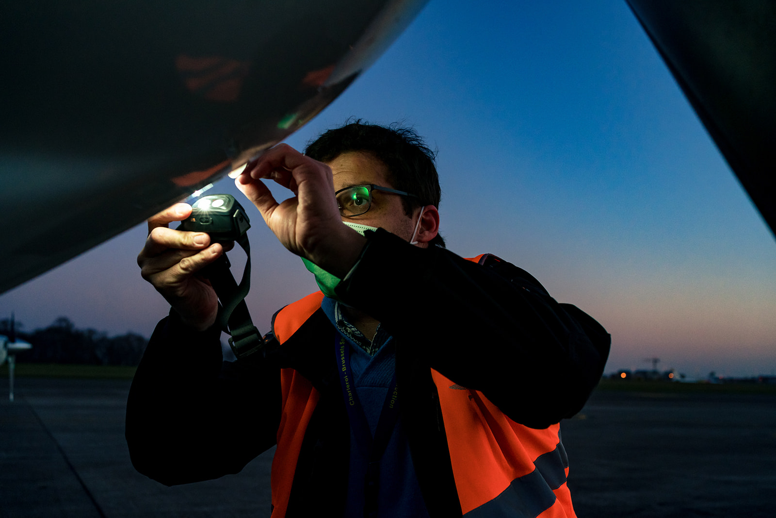 Un pilote regarde dans une trape du fuselage d'un avion avec une lampe frontale pendant le reportage photo
