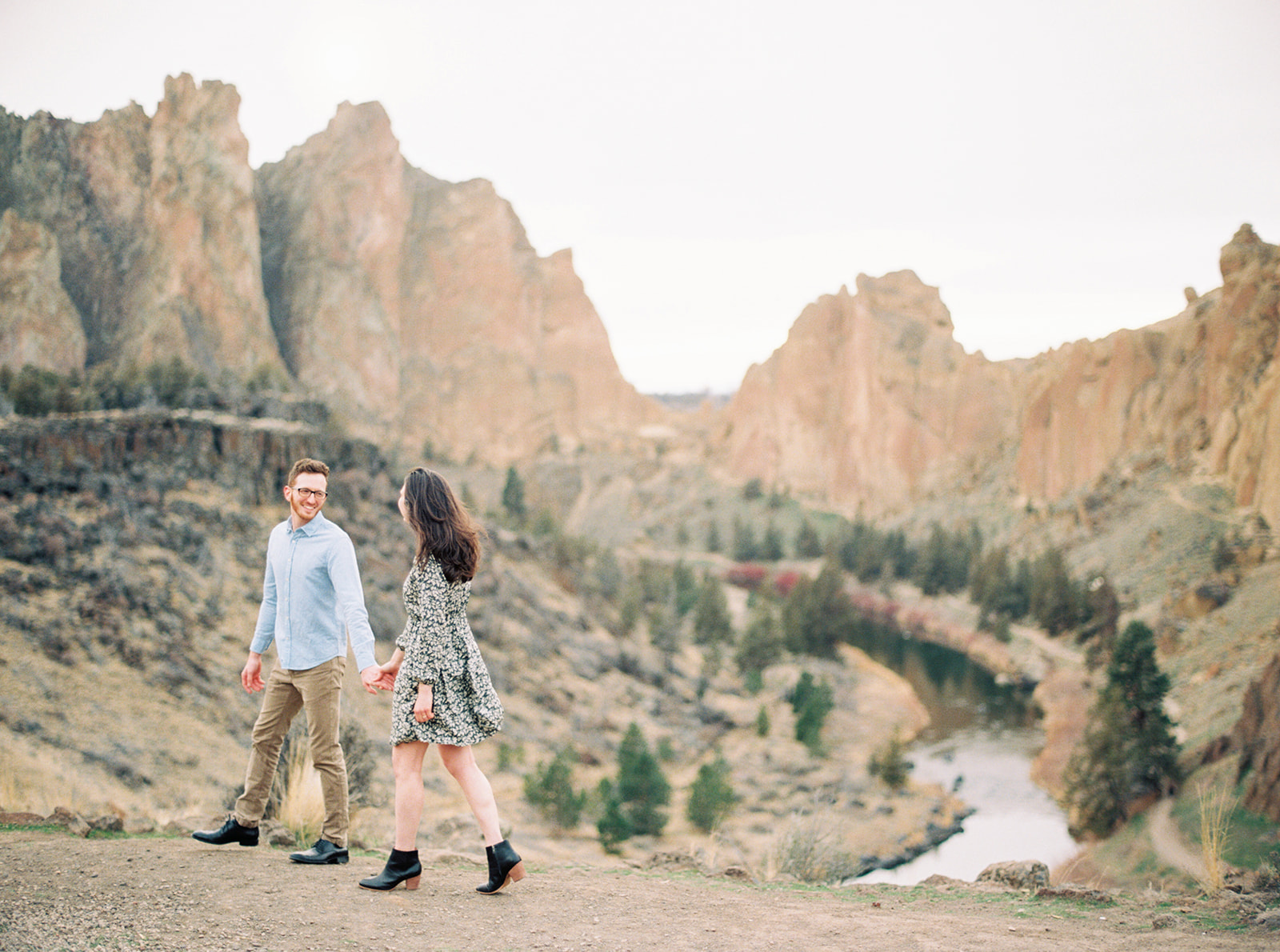 a couple walks hand-in-hand with Smith Rock behind them