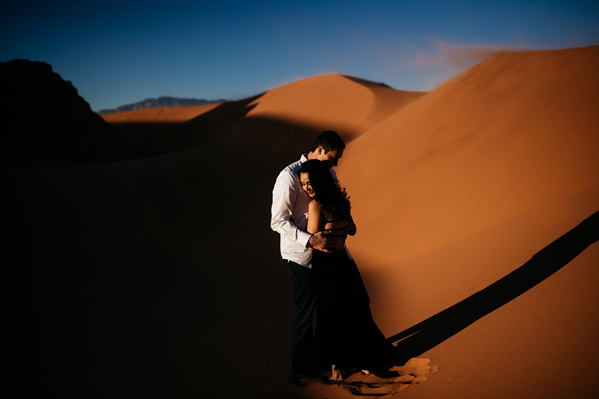 cinematic moment of a couple's dramatic embrace standing in the shadow of a sand dune