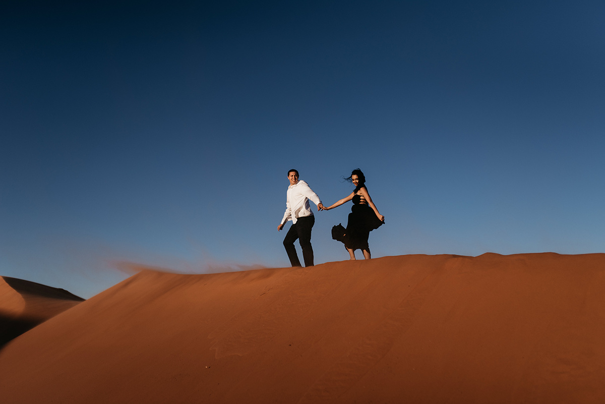 couple runs across the red utah sand dunes as the wind blows the sand