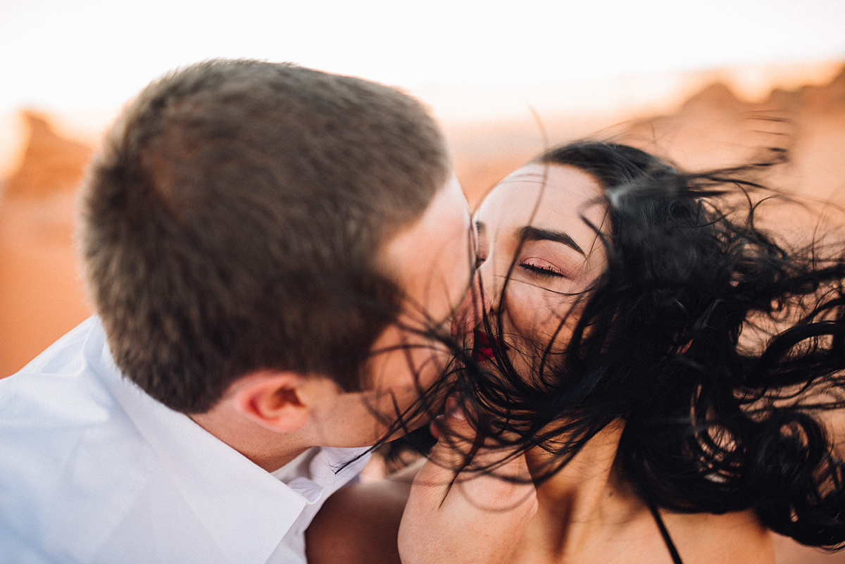a couple shares a kiss in vibrant color, with her hair wildly dancing in the wind