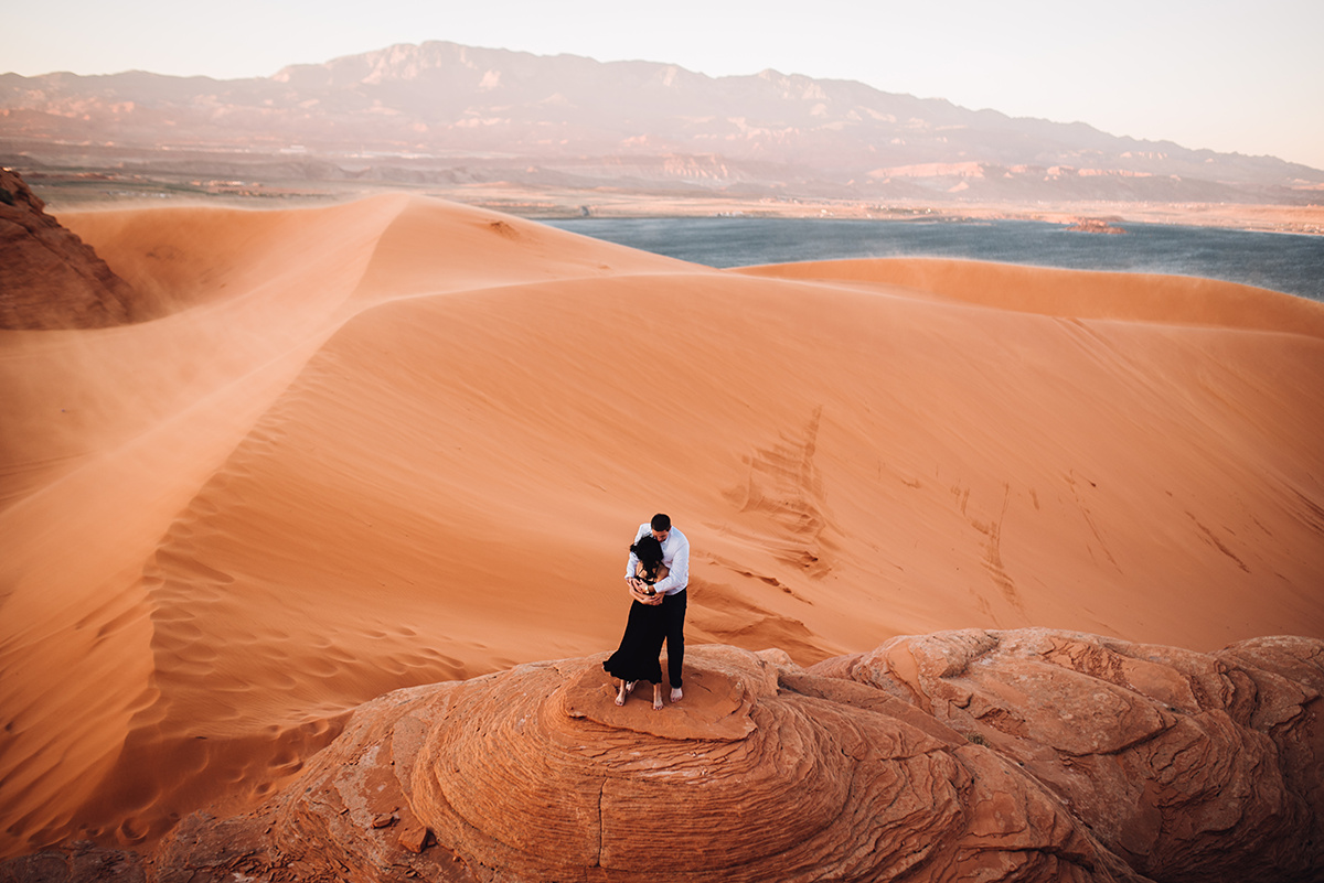 couple standing on a red rock amongst red sand dunes