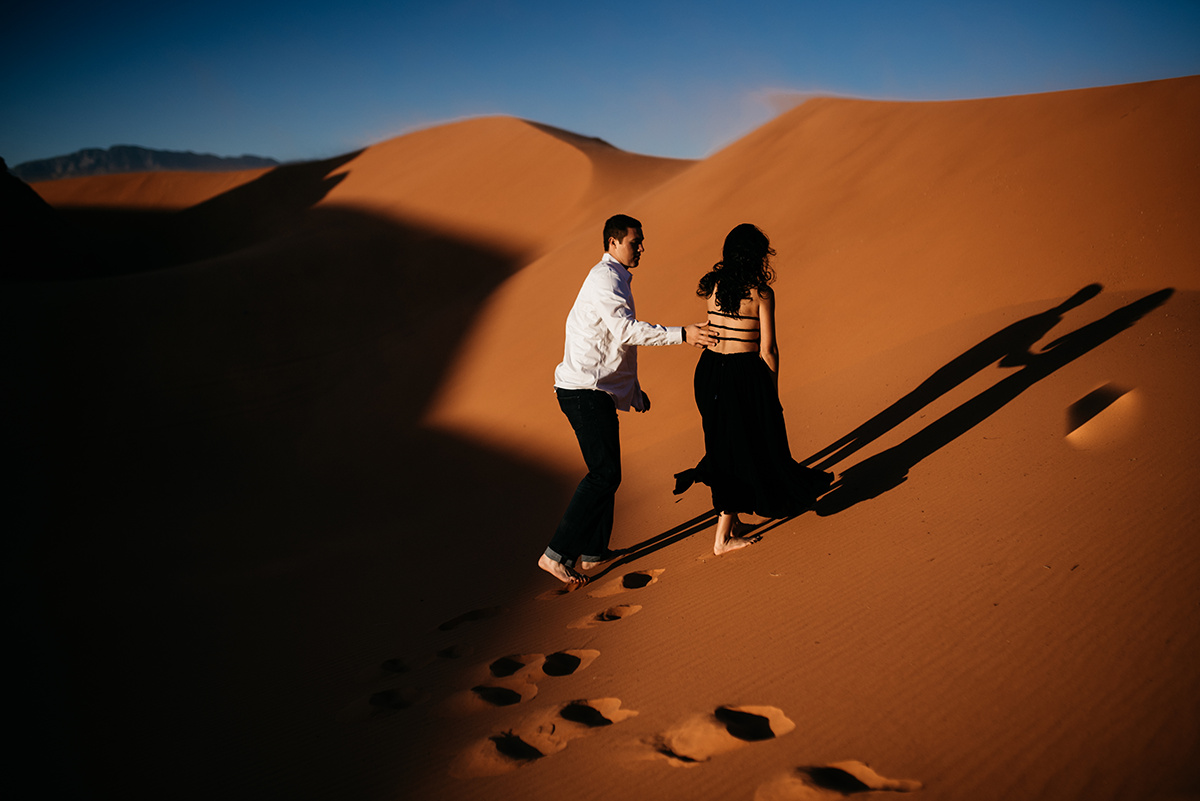 couple walking up a red sand dune together featuring bold, dramatic editing