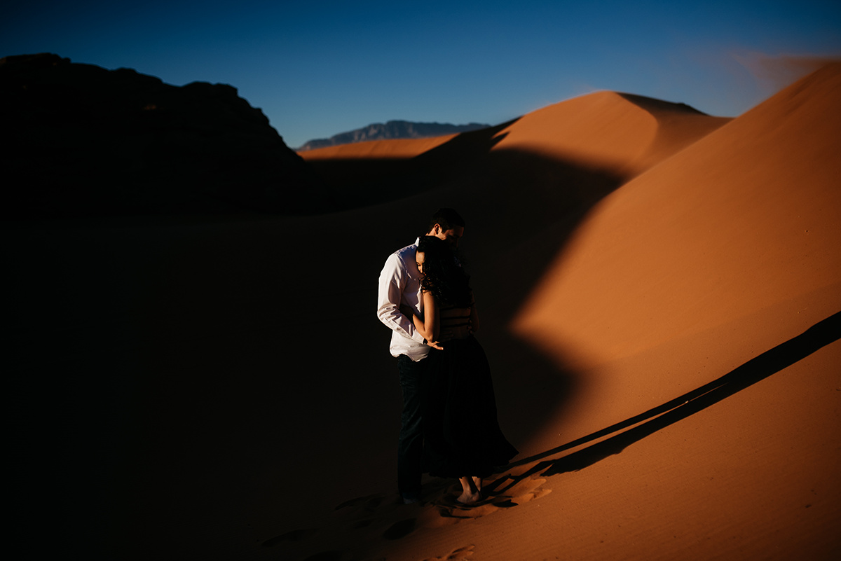 a couple's dramatic embrace standing in the shadow of a sand dune, showcasing emotive posing