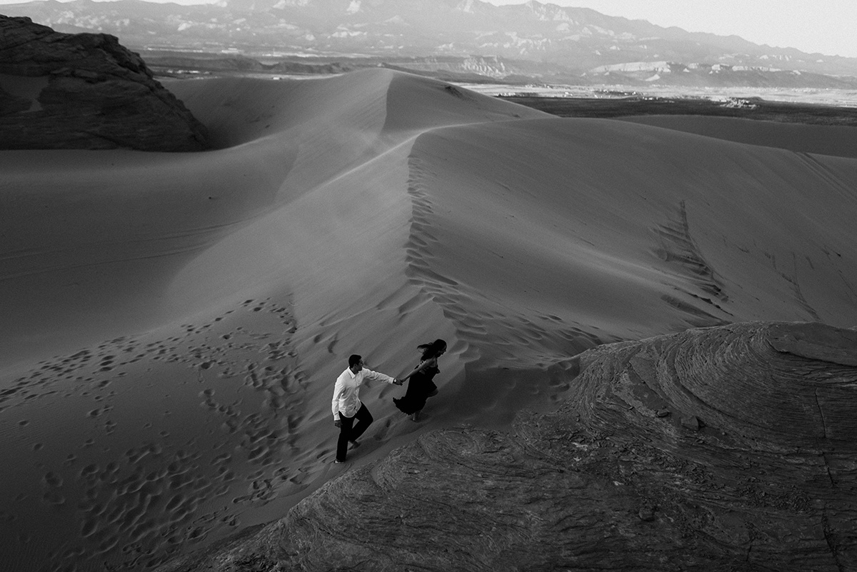 drone shot of a couple walking up a sand dune as they hold hands