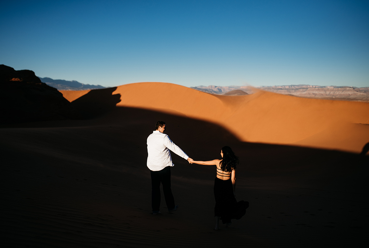 an emotive couple holding hands walking though the red sand dunes in cinematic, dramatic light