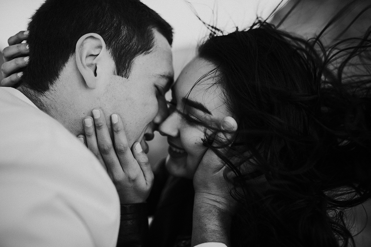 Faces draw close for a kiss in bw, her hair wildly dancing in the wind, echoing their untamed, passionate lov