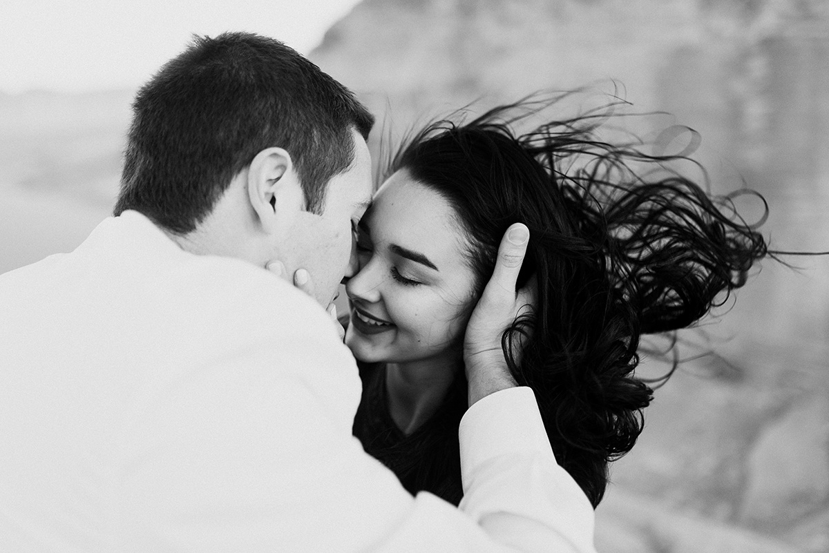 Faces draw close for a kiss in bw, her hair wildly dancing in the wind, echoing their untamed, passionate lov