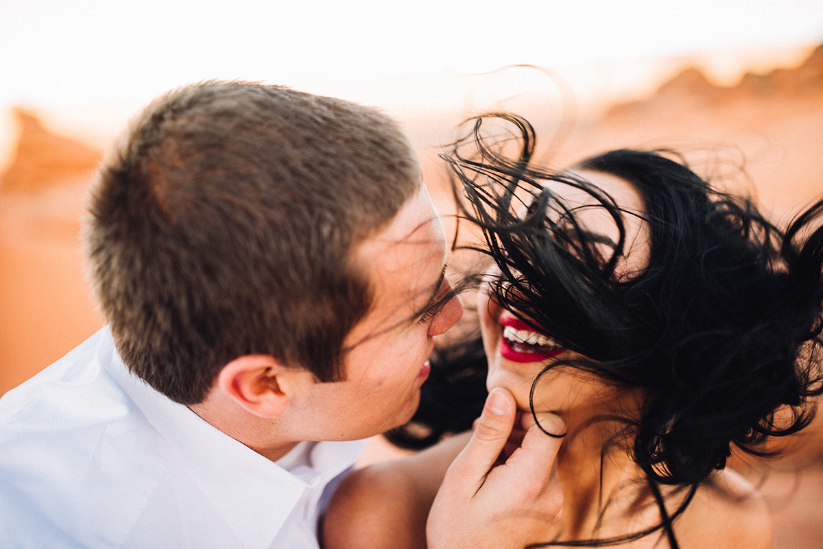 Faces draw close for a kiss in vibrant color, as she laughes with her hair wildly dancing in the wind