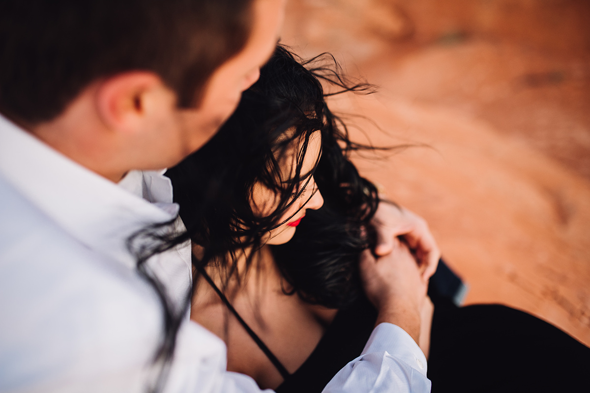 he holds her closely in an emotive embrace sitting on the red rocks in utah