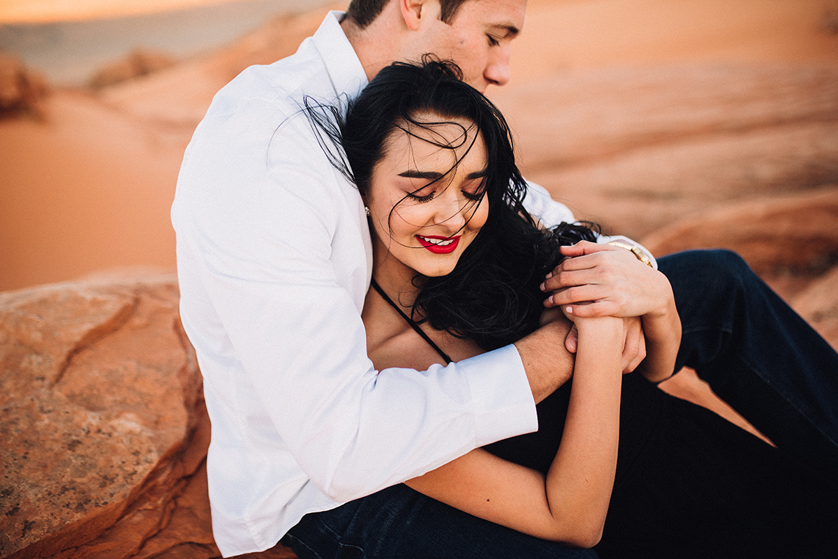 she smiles as her hold her closely in an emotive embrace sitting in the colorful red sand dunes