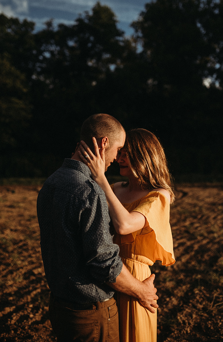 close shot, intimate moment between a couple embracing with foreheads together in direct light standing in a dirt field