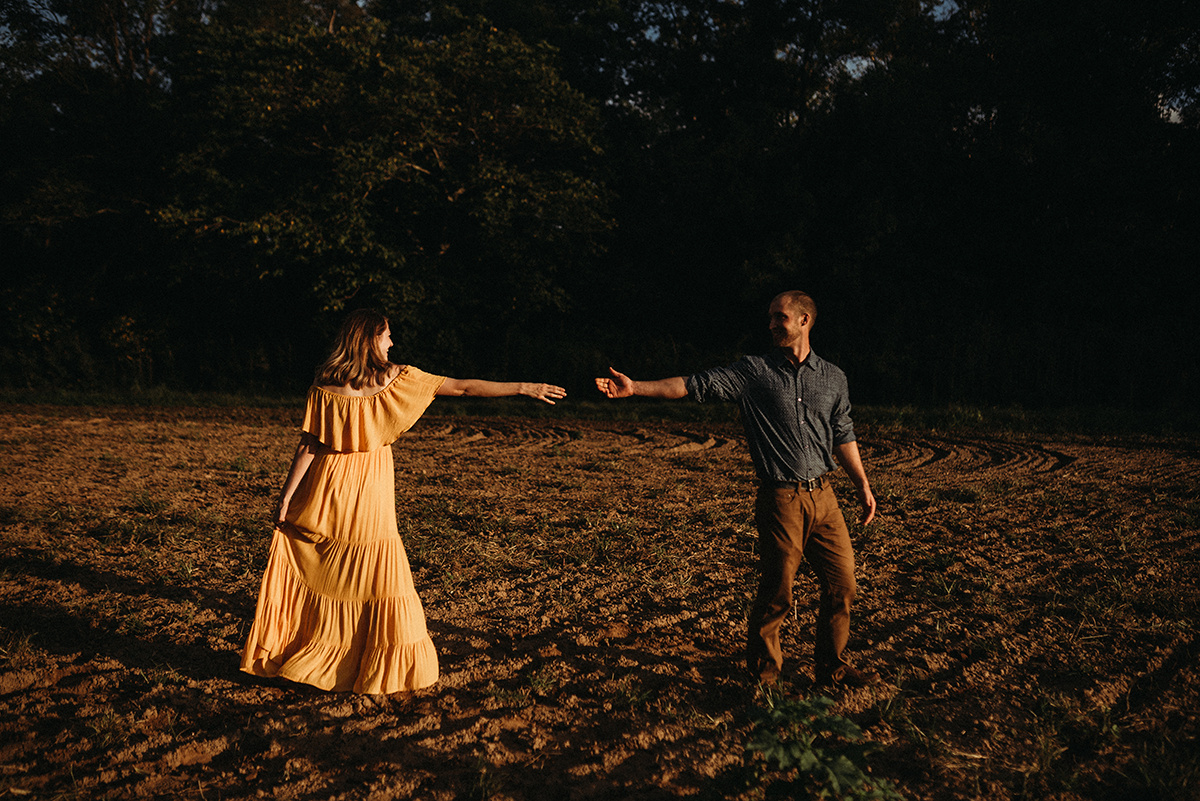 couple reaching for one another in direct light standing in a dirt field