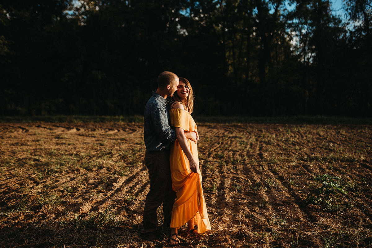 emotive moment of a man embracing his wife and kissing her neck in direct sunlight standing in a dirt field