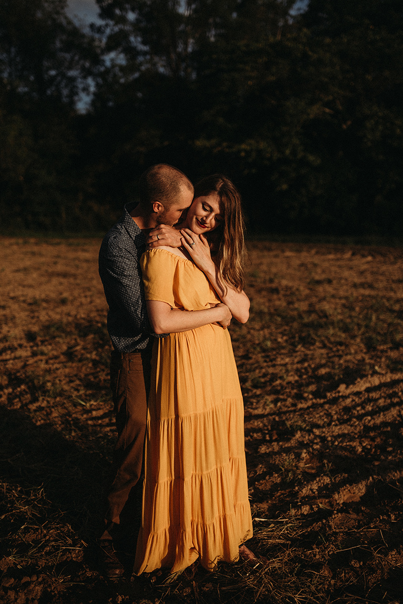 emotive moment of a man embracing his wife and kissing her neck in direct sunlight standing in a dirt field