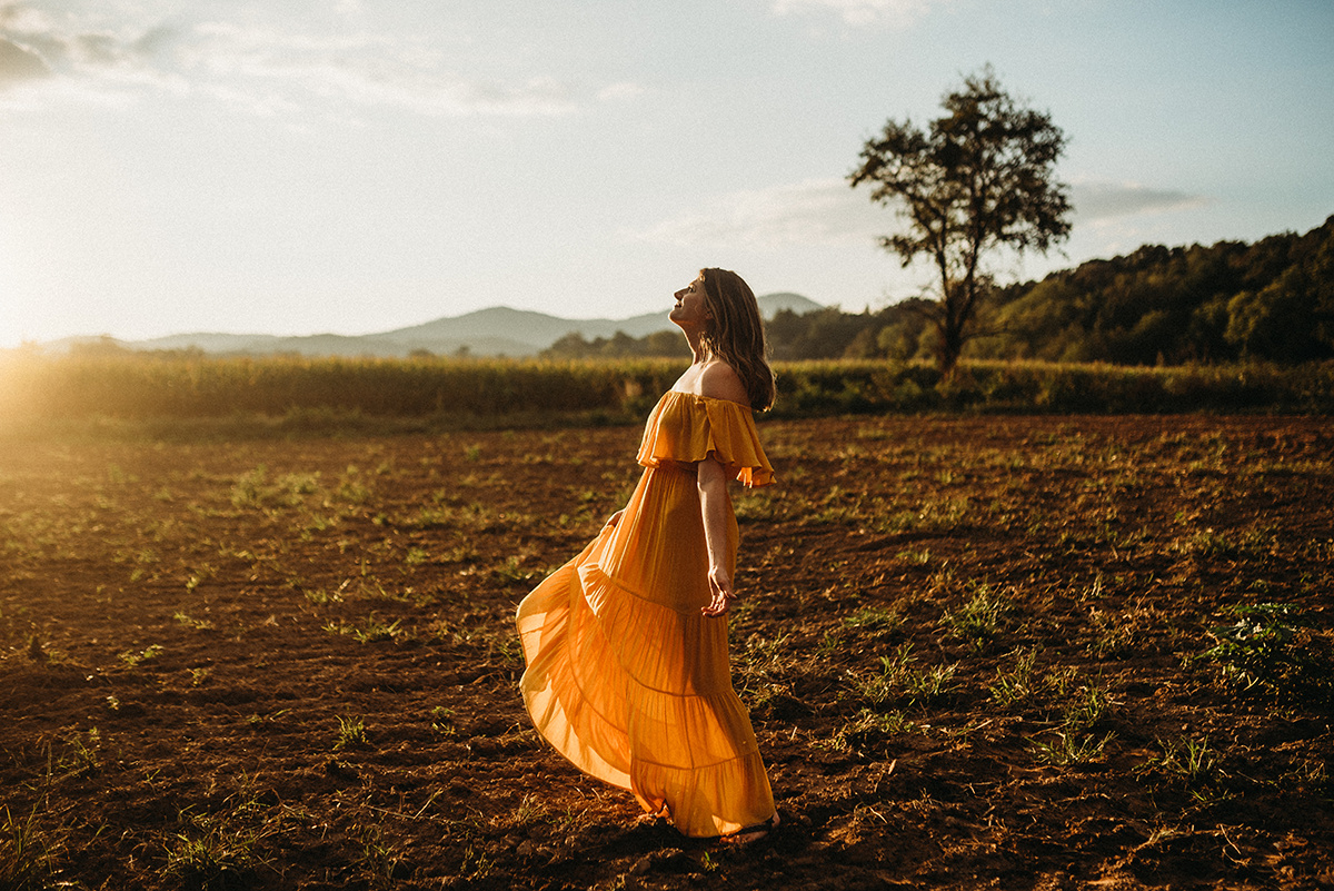 emotive photo of a mother holding her head back walking in a dirt field drenched in beautiful golden backlight