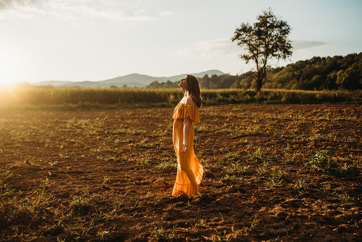 emotive photo of a mother holding her head back walking in a dirt field drenched in beautiful golden backlight