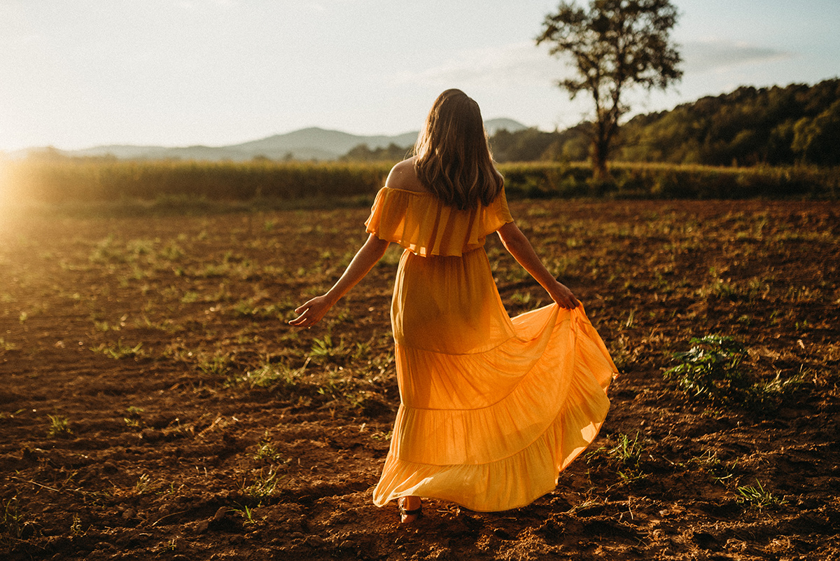 emotive photo of a mother holding her yellow dress dancing in a dirt field drenched in beautiful golden backlight