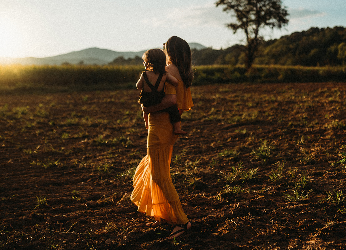 emotive photo of a mother holding young child walking in a dirt field drenched in beautiful golden backlight