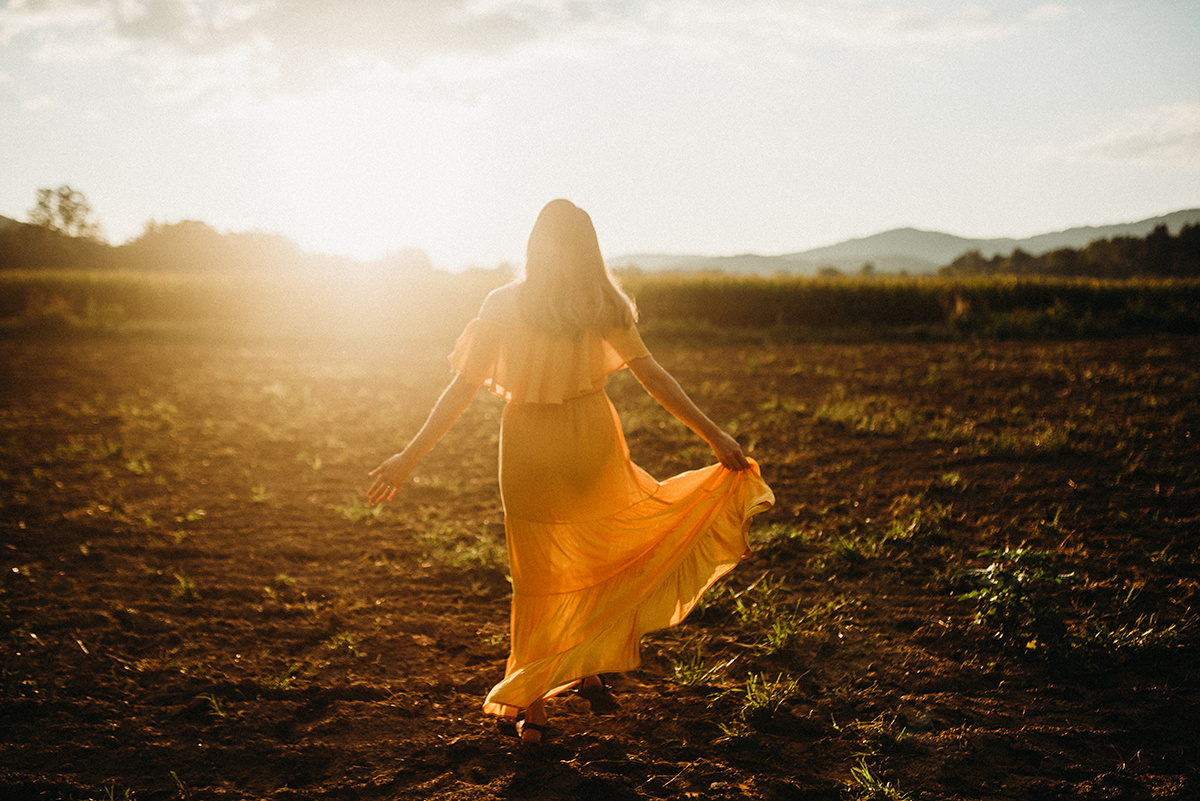 emotive photo of a mother wearing a yellow dress dancing in a dirt field drenched in beautiful golden backlight