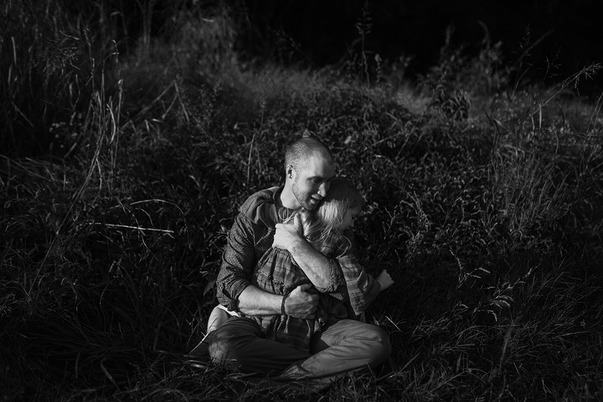 father and daughter sharing an emotive embrace in bw sitting in tall grass